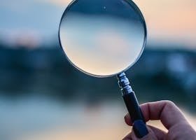 A magnifying glass held by a hand outdoors at sunset, focusing on exploration.